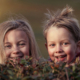 Zwei lachende Kinder die halb hinter eine kleinen Hecke stehen.