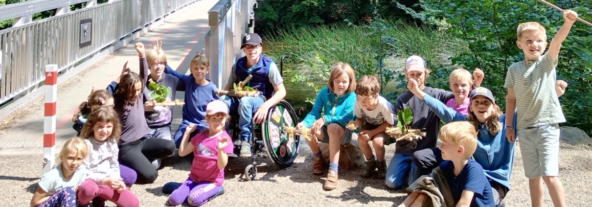 Kindergruppe auf einer Sandfläche neben einer Brücke. Gruppenfoto Naturforschercamp 2024.