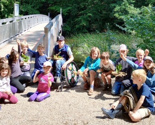 Kindergruppe auf einer Sandfläche neben einer Brücke. Gruppenfoto Naturforschercamp 2024.