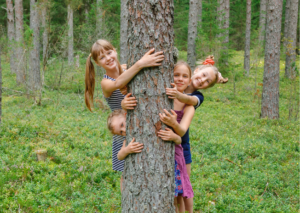 Vier Kinder die sich im Wald hinter einem Baum verstecken.